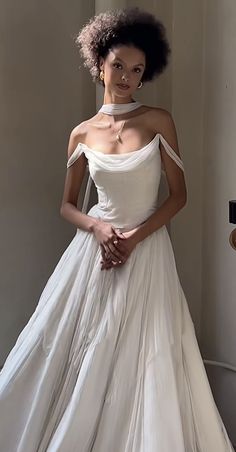 a woman in a white dress standing next to a wall with her hands on her hips