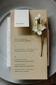 a white plate topped with a piece of paper next to a flower on top of it