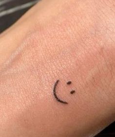 a small black smiley face tattoo on the arm