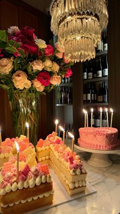 a table topped with cakes and candles next to a vase filled with flowers on top of a counter