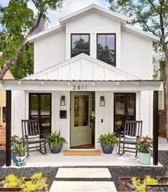 a white house with two rocking chairs on the front porch and potted plants outside