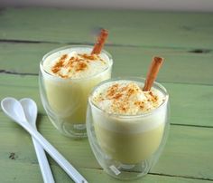 two glasses filled with drinks sitting on top of a wooden table next to spoons