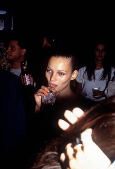 a woman drinking from a glass in front of a group of people at a party