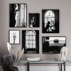 black and white photographs hang on the wall next to a table with a vase in front of it