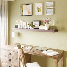 a wooden desk topped with a laptop computer next to a wall filled with framed pictures