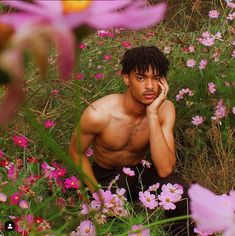 a shirtless man sitting in a field of flowers