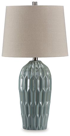 a table lamp with a beige shade on the base and a light blue ceramic vase