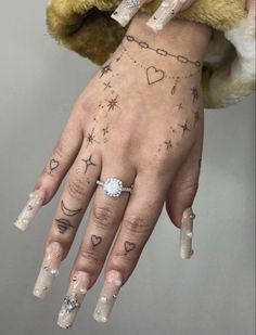 a woman's hand with tattoos and rings on her left hand, holding onto a teddy bear