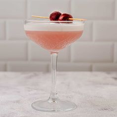 a pink cocktail in a coupe glass with cherries on the rim and garnish