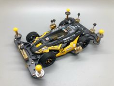 a toy race car with yellow wheels on a gray surface and some black screws