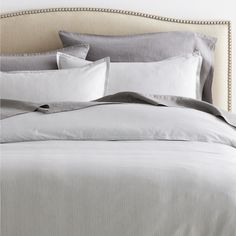 a bed that has some pillows on top of it and is made up with grey linens