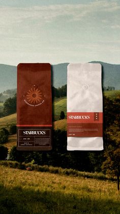 two coffee bags sitting on top of each other in front of a green field and mountains