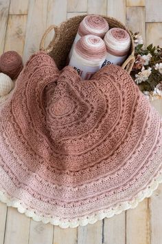 a crocheted blanket and two balls of yarn in a basket on a wooden floor