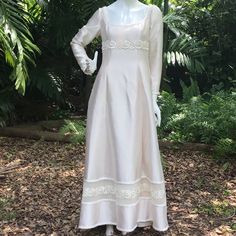 a white dress is on display in front of some trees and bushes, with one woman's head turned to the side