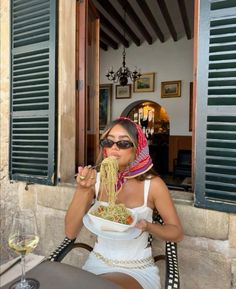 a woman sitting at an outdoor table eating food with a glass of wine in front of her