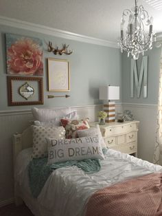 a white bed sitting under a chandelier next to a window in a bedroom