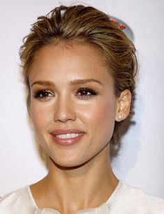 a close up of a person wearing a white dress and smiling at the camera with her hair in a bun