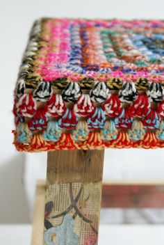 a multicolored stool with wooden legs and fabric on it's seat cover