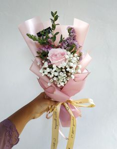 a person holding a bouquet of flowers with a ribbon tied around the end and some writing on it