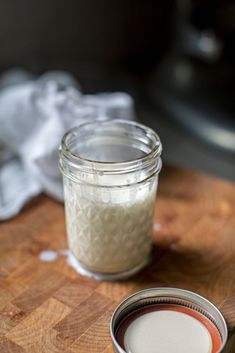 a wooden cutting board topped with a glass jar filled with white liquid next to a metal container