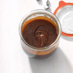 a jar filled with brown sauce sitting on top of a white table next to two spoons