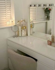 a white desk with a mirror and some bottles on it next to a flower vase