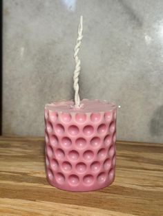 a pink candle sitting on top of a wooden table next to a white string hanging from it's end