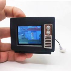 a hand holding up a small black and silver video game controller with a house on the screen