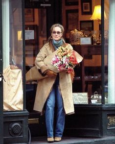 a woman is walking out of a store with flowers in her hand