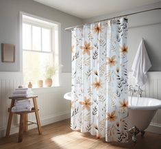 a white bath tub sitting under a window next to a shower curtain with flowers on it