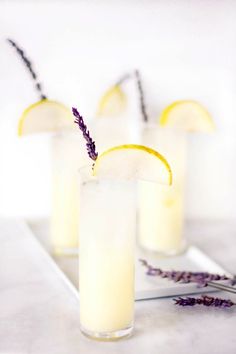 three glasses filled with lemonade sitting on top of a white counter next to lavender flowers