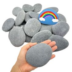 a hand holding a rock with a rainbow painted on it, surrounded by other rocks