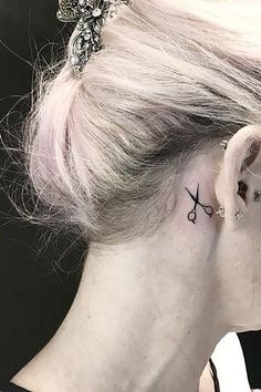 a woman with a small tattoo on her left side behind the ear is wearing a pair of scissors