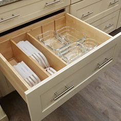 an open drawer in a kitchen filled with empty glasses and silverware on the counter