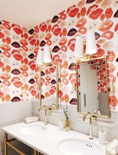 a white sink sitting under two mirrors next to a wall covered in red lipstick prints