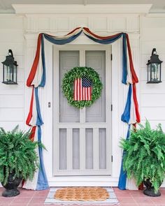 an american flag wreath on the front door of a white house with potted plants