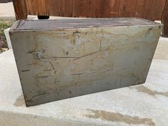 an old metal box sitting on top of a cement slab in front of a wooden fence