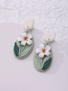 two white flowers are attached to some green and white ear wires on a white surface