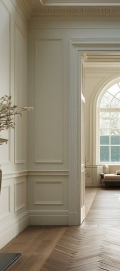 an open door leading to a living room with white walls and wood floors, along with a vase filled with flowers