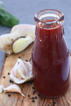 a jar filled with sauce sitting on top of a wooden cutting board next to garlic