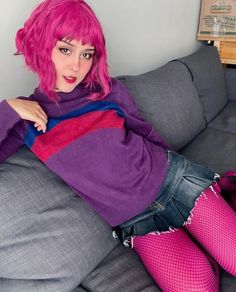 a woman with pink hair is sitting on a couch wearing fishnet stockings and tights