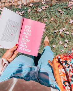 a person sitting on the ground holding a book in their hands and looking down at it