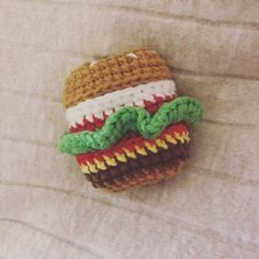 a crocheted hamburger brooch sitting on top of a bed