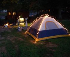 a tent is lit up with fairy lights and sits in the middle of a field