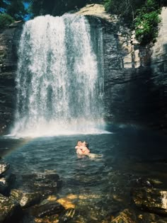 a person swimming in the water under a waterfall