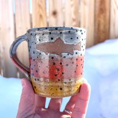 a hand holding a coffee cup that has been painted with different colors and shapes on it