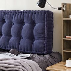 a blue headboard sitting on top of a bed next to a book shelf and lamp