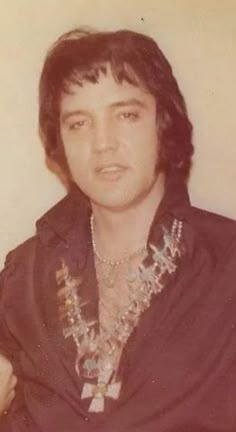 an old photo of a man with long hair and necklaces on his chest, wearing a black shirt