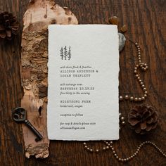 the wedding stationery is laid out on a wooden table with pine cones and beads