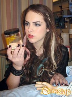 a woman sitting on a bed holding a jar and looking at the camera with one hand